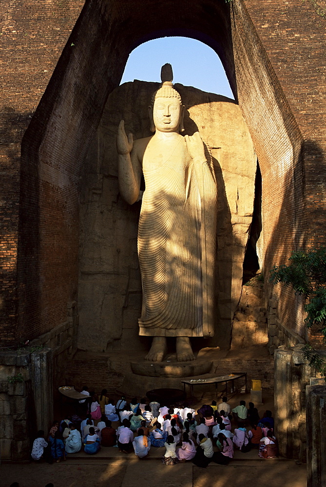 Pilgrims seated in front of the 39 ft high standing Buddha, Aukana, Sri Lanka, Asia