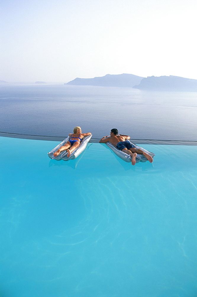 Holidaymakers on lilos in pool looking across bay, Oia, Santorini (Thira), Greek Islands, Greece, Europe