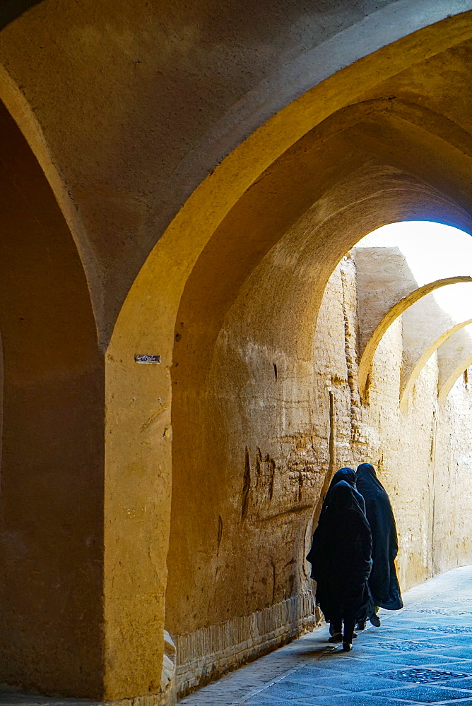 Three women in chadors hurrying down typical vaulted alleyway, Yazd, Iran, Middle East