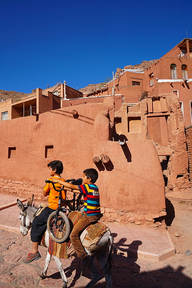 Boy with donkey gives bicyclist a lift in 1500 year old traditional village of red mud brick houses, Abyaneh, Iran, Middle East