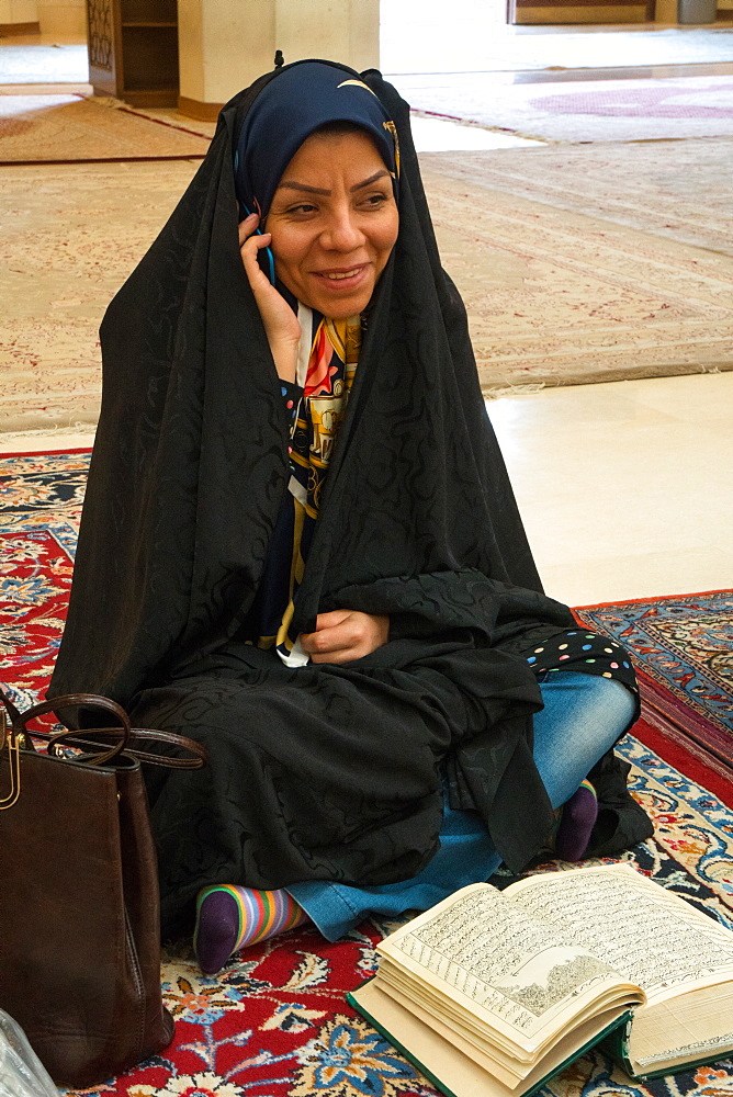 Young woman torn between her mobile and her religious reading, Aramgah-e Shah-e Cheragh (Mausoleum of the King of Light), Shiraz, Iran, Middle East