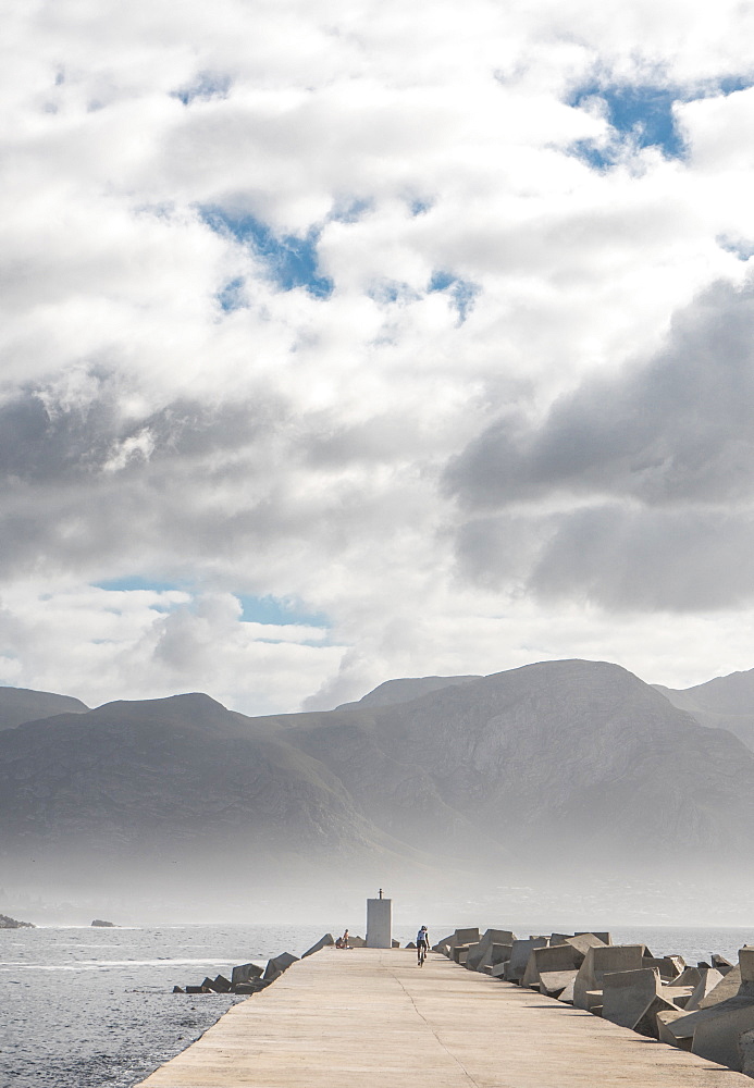 As sun breaks early morning mist, cyclist at the end of the pier, New Harbour, Hermanus, South Africa, Africa