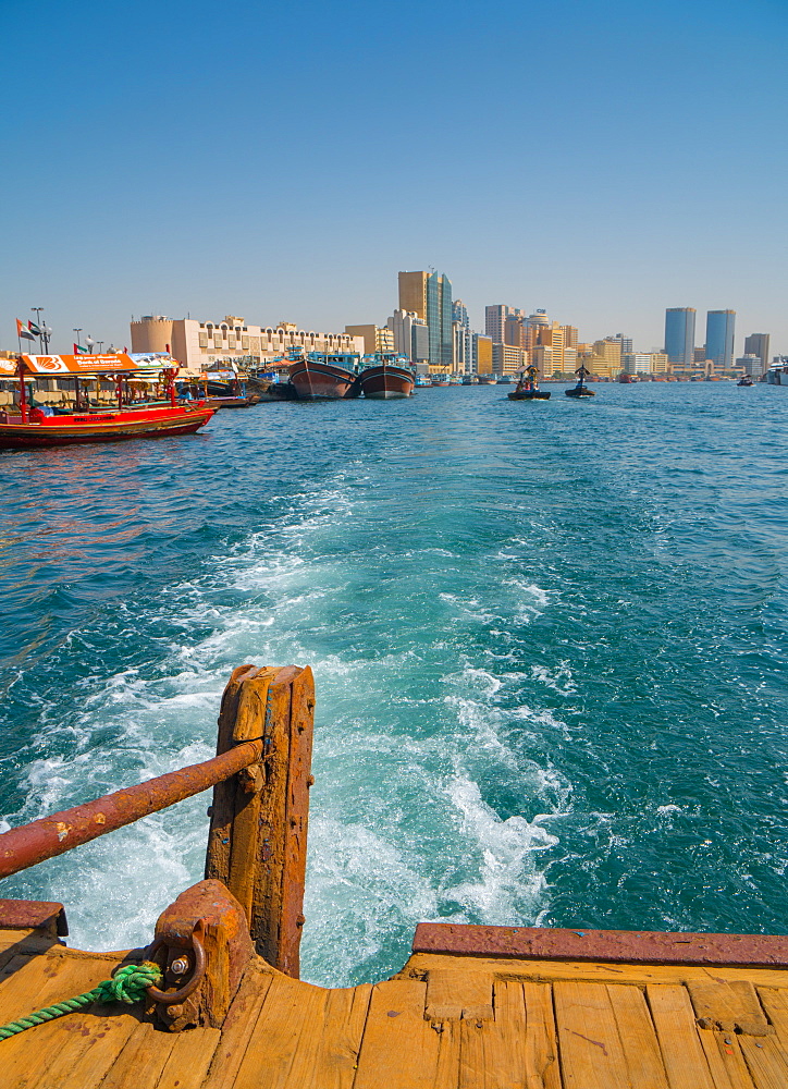 Modern Dubai cityscape disappears in the wake of an old water taxi speeding past the dhow harbour up Dubai Creek, Dubai, United Arab Emirates, Middle East