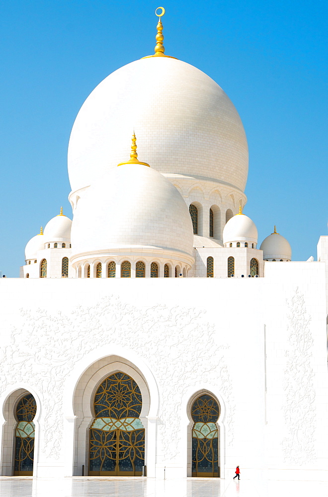 Interior of Sheikh Zayed Grand Mosque, brilliant white of marble buildings punctuated by tiny woman in red, Abu Dhabi, United Arab Emirates, Middle East