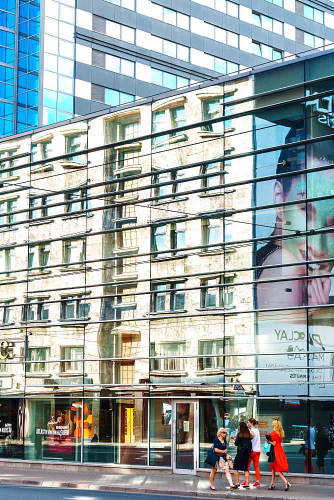 Building reflections with women in brightly coloured dresses on sidewalk near Galeria Riga, Riga, Latvia, Europe