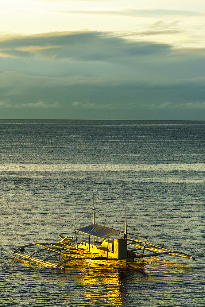 A lone bangka (outrigger canoe) bathed in warm dawn light berthed by Panglao Beach, Bohol Island, Philippines, Southeast Asia, Asia