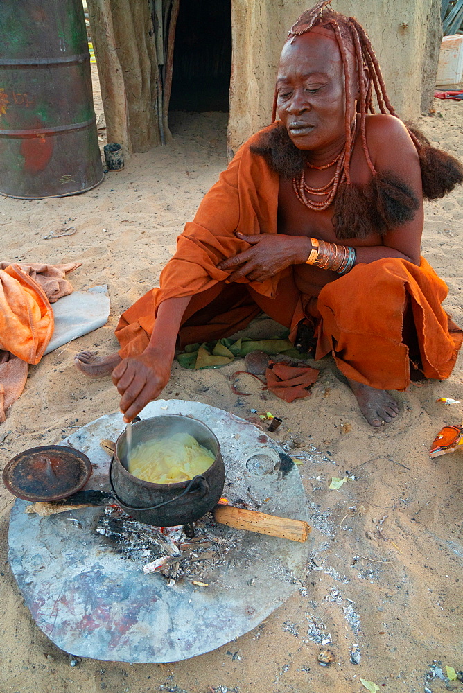 One senior red ochred Himba woman cooking her meal on an open fire, Puros Village, near Sesfontein, Namibia, Africa