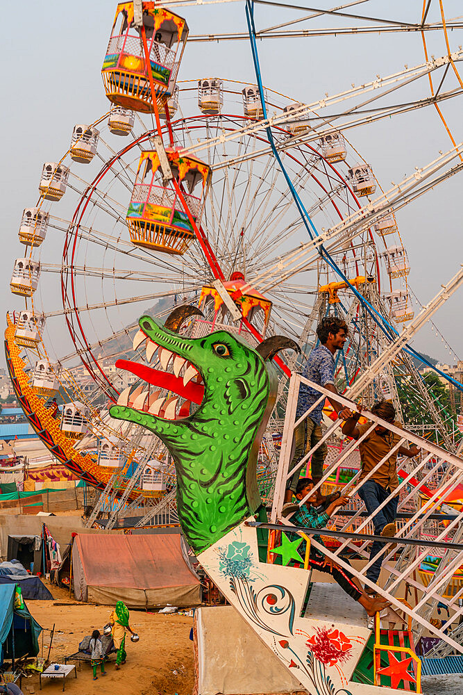 Fairgoers wait for a swinging gondola to start with two Ferris wheels in the background, Pushkar Fair, Rajasthan, India, Asia