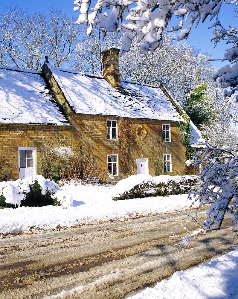 Cotswold farmhouse beside a road covered in snow in winter in England 