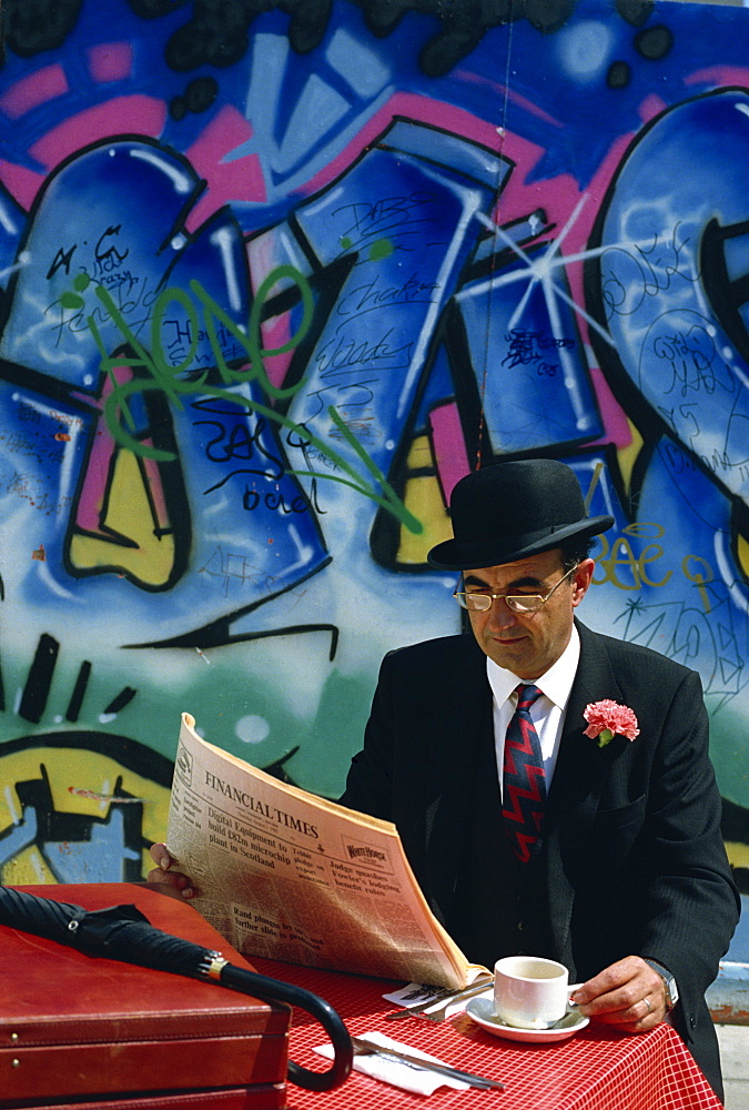 Businessman wearing suit and bowler hat reading newspaper with coffee, London, England, United Kingdom, Europe