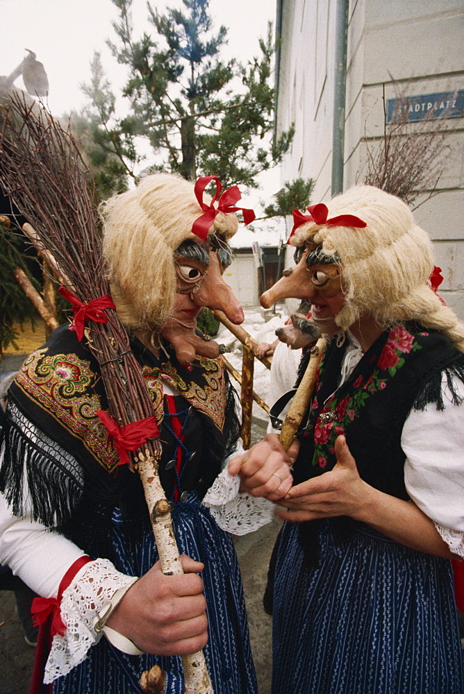 Two people wearing masks and traditional dress, one carrying a broomstick, in the Fasnacht carnival in Imst, Austria, Europe