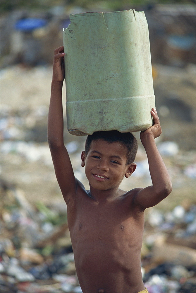 Boy carrying container on head on rubbish strewn beach, Dominican Republic, West Indies, Caribbean, Central America