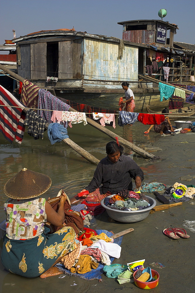 Women washing their laundry on bank of the Ayeryarwady (Irrawaddy) River, with wooden boat in background, Mandalay, Myanmar (Burma), Asia