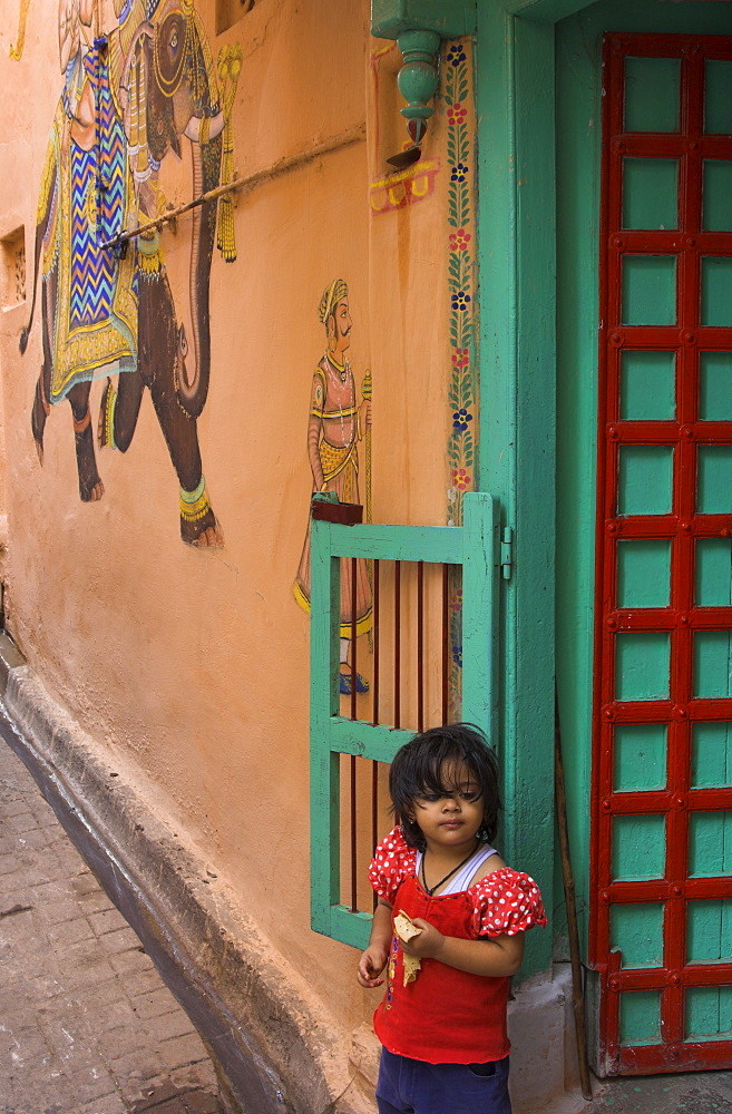 Small girl standing in doorway of typical house decorated with Mewar folk art, Jagdish Mandir area, old city, Udaipur, Rajasthan state, India, Asia