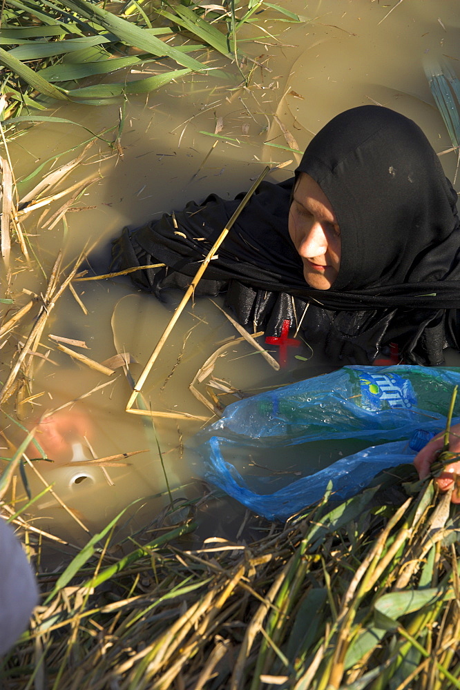 Portrait of a Russian nun in the water blessing and filling water bottle with river water, Christian Orthodox ceremony at Epiphany, River Jordan, Qasr el Yahud, Israel, Middle East