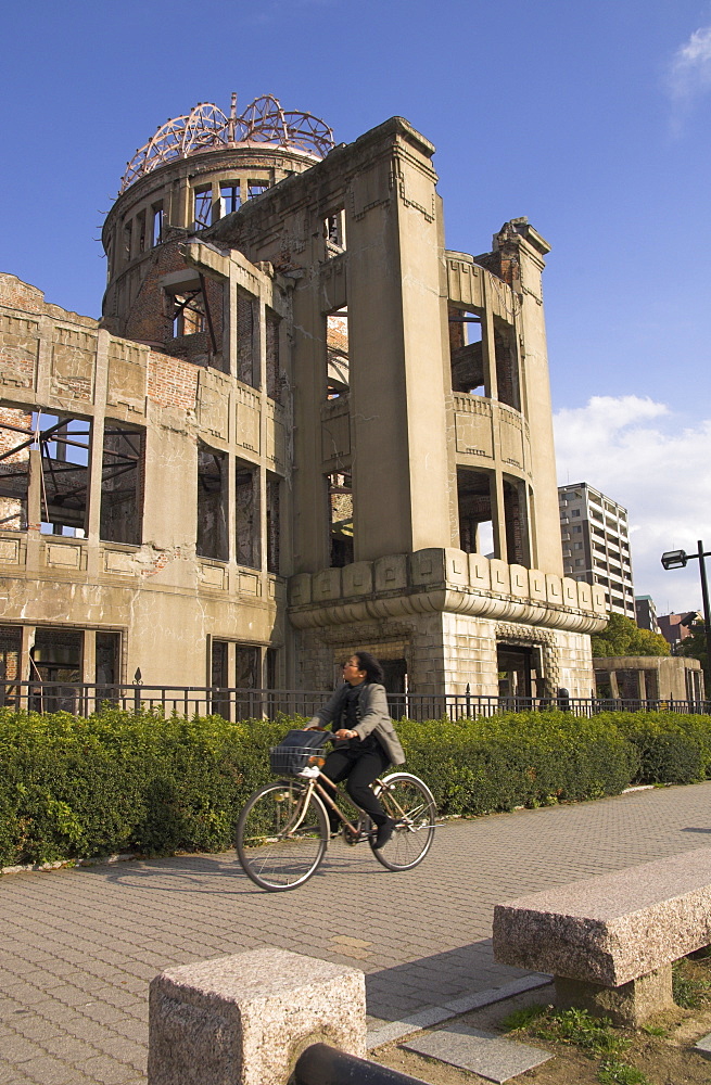 Woman riding bicycle past A Bomb Dome, the ruins of the Industrial Promotion Hall destroyed by the atomic bomb of 6 August 1945, UNESCO World Heritage Site, Hiroshima, Honshu, Japan, Asia