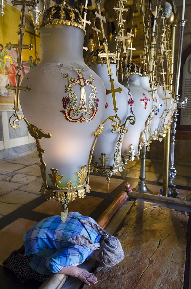 Close up of traditional lamps hanging above the Stone of Anointing with woman prostrating, Church of the Holy Sepulchre, Old City, Jerusalem, Israel, Middle East