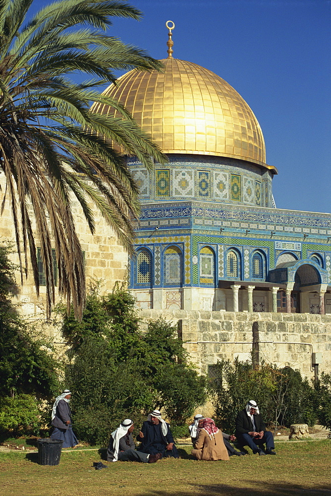 A group of Arab men sit on the grass on Temple Mount, with the gold Dome of the Rock in the background, in the Old City of Jerusalem, Israel, Middle East