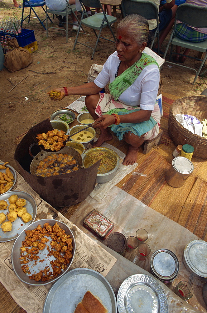 High angle view of an Indian woman sitting cooking onion bhajis for sale at a food stall in a market, Goa, India, Asia