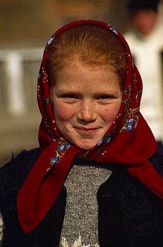 Head and shoulders portrait of a young Romanian girl with red hair wearing a red head scarf, smiling and looking at the camera, in Bottiza village, Romania, Europe