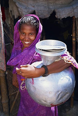 Portrait of a smiling Bangladeshi girl in a purple sari, looking at the camera, carrying a large water pot in a slum Bangladesh, Asia