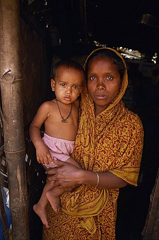 Portrait of a Bangladeshi mother in a sari holding her young child, looking at the camera, in a slum in Dhaka, Bangladesh, Asia