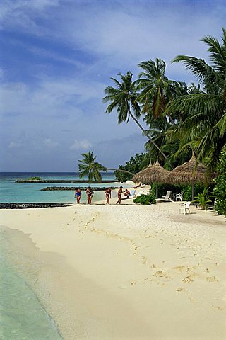 Women on the beach with thatched umbrellas and palm trees at Nakatchafushi on the Maldive Islands, Indian Ocean, Asia