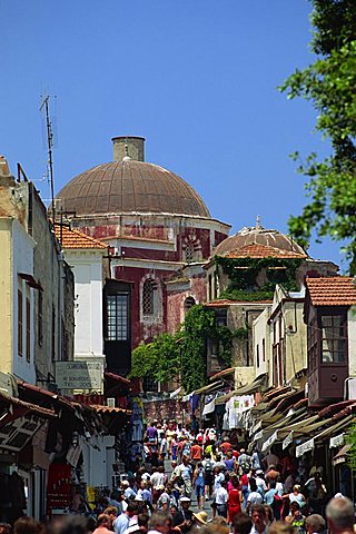 Tourists in busy back street with church dome behind, in the old town, Rhodes Town, Rhodes, Dodecanese Islands, Greek islands, Greece, Europe