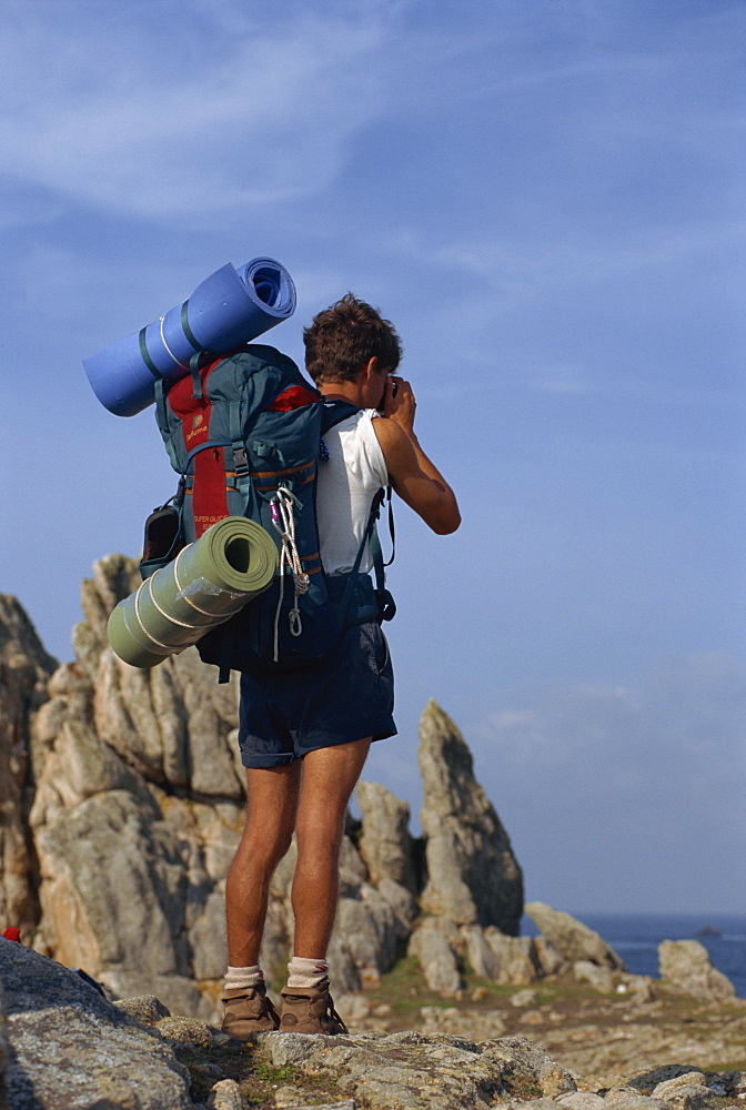 Portrait of the back view of a backpacker with bedding rolls and rucksack on Ouessant island in Brittany, France, Europe