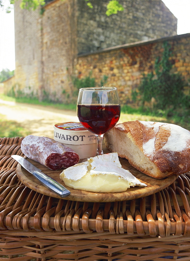 Still life of bread, glass of red wine, cheese and sausage, picnic meal on top of a wicker basket, in the Dordogne, France, Europe