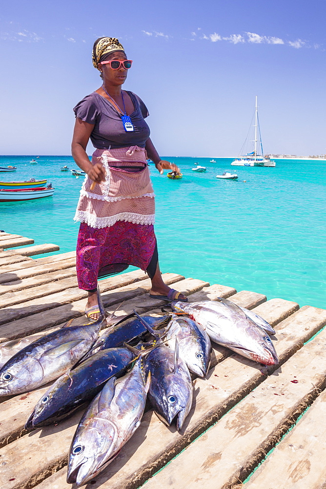 Colourful local woman selling freshly caught yellow fin tuna fish from the pier at Santa Maria, Sal island, Cape Verde, Africa