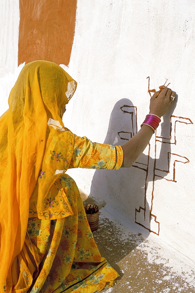 Woman painting design on a wall in a village near Jaisalmer, Rajasthan state, India, Asia