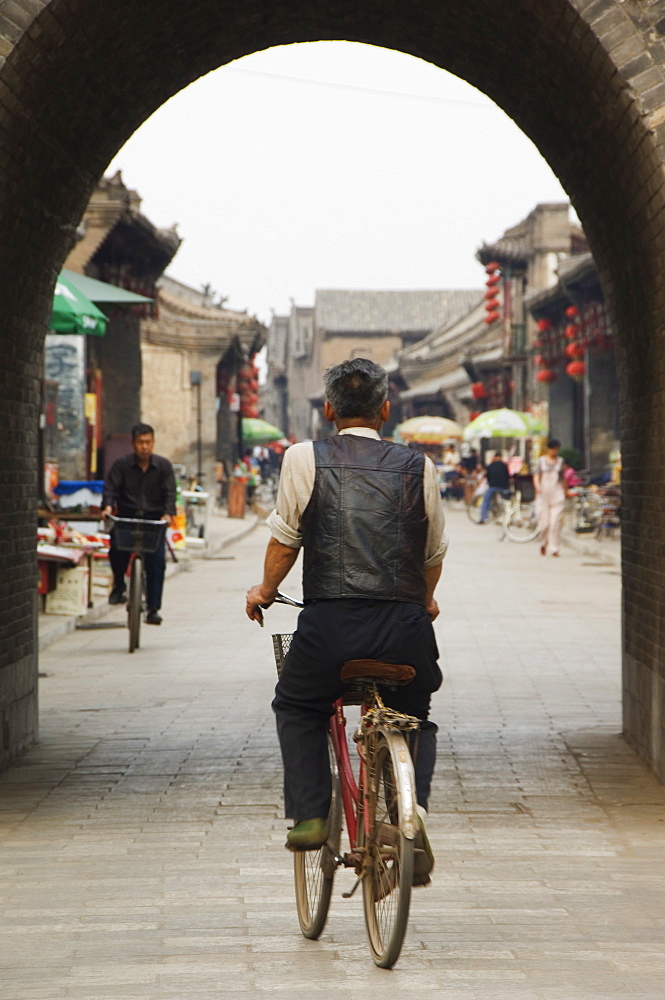 A man cycling though an arched street in the historic center of Pingyao, UNESCO World Heritage Site, Shanxi Province, China, Asia