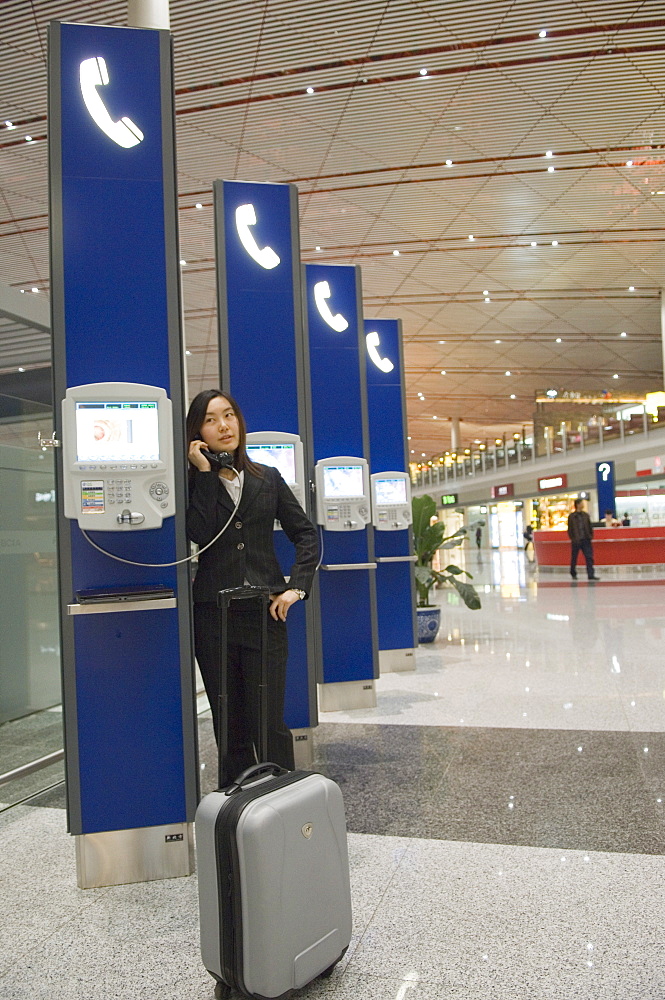 A Chinese business woman making a telephone call at Beijing Capital Airport part of new Terminal 3 building opened February 2008, second largest building in the world, Beijing China, Asia