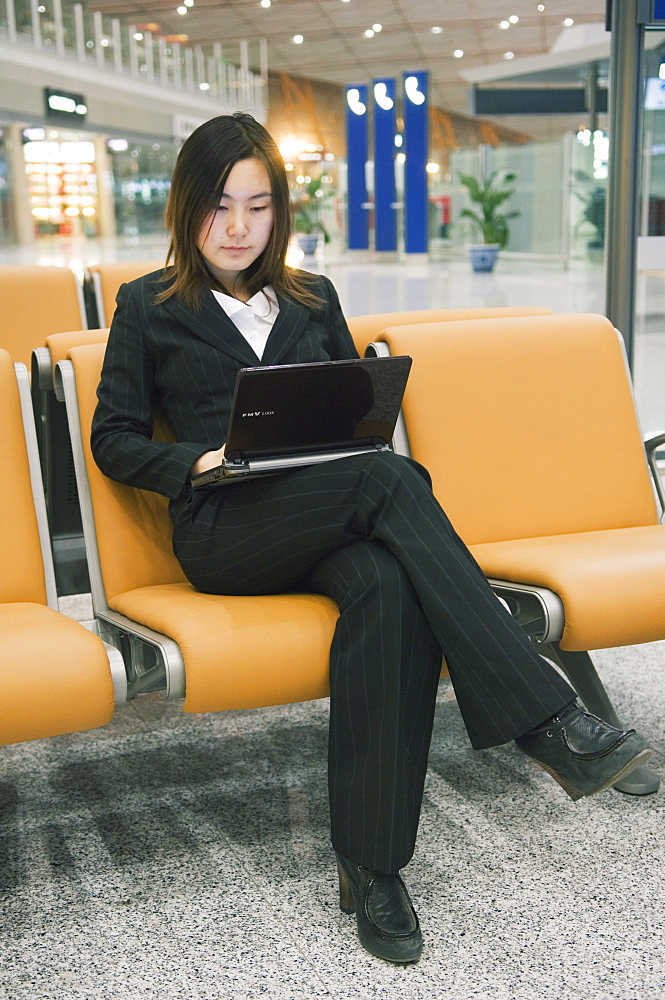 A Chinese business woman using a laptop computer at Beijing Capital Airport part of new Terminal 3 building opened February 2008, second largest building in the world, Beijing China, Asia