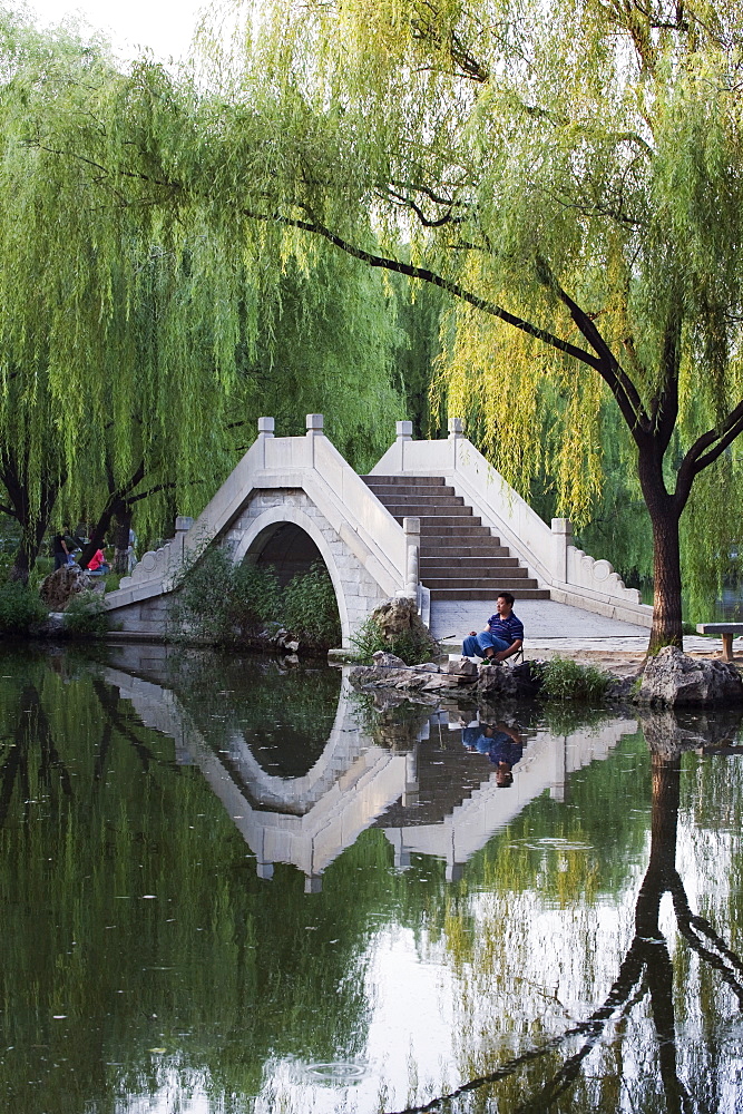 Man fishing next to a stone arched bridge in Zizhuyuan Black Bamboo Park, Beijing, China, Asia