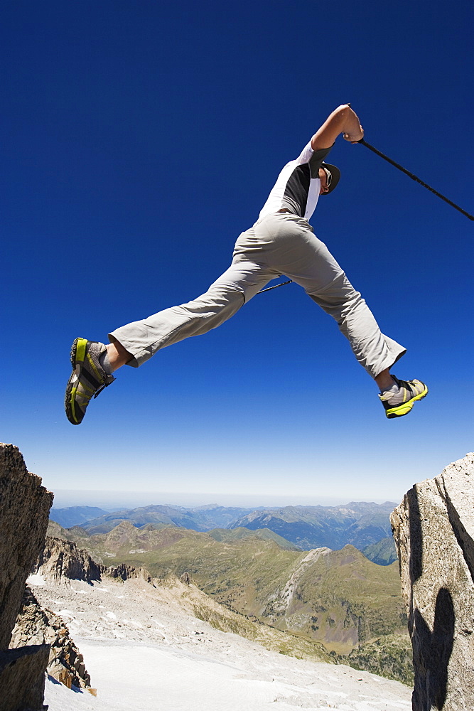 Hiker jumping across a gap in the rocks, Pico de Aneto, the highest peak in the Pyrenees, Spain, Europe