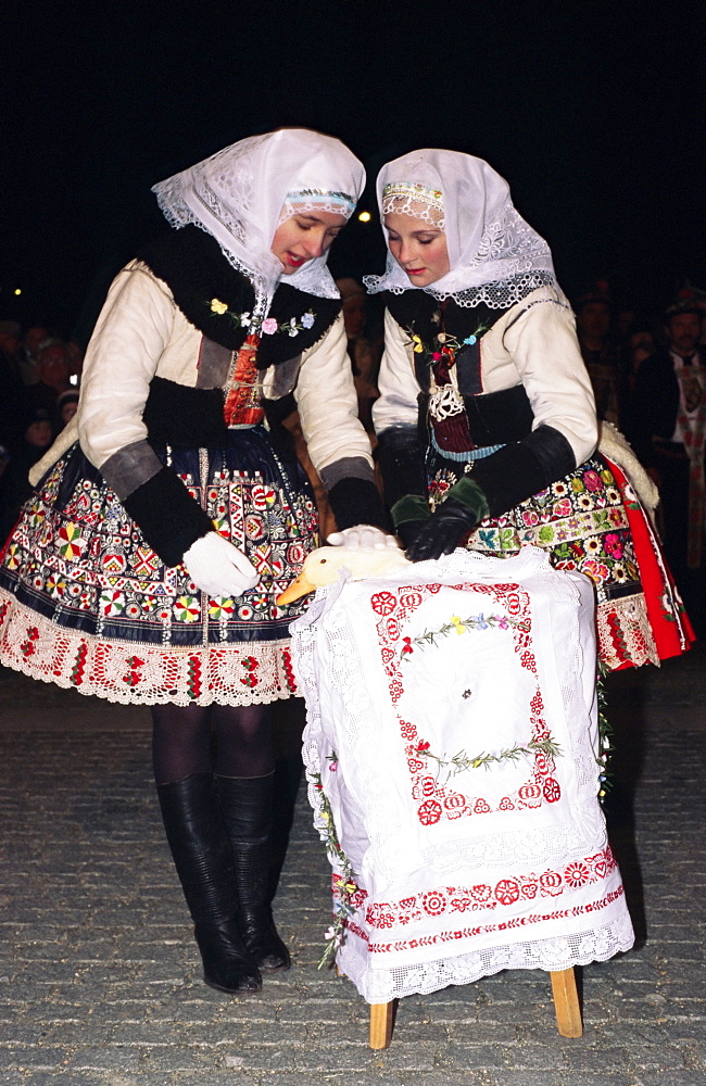 Two girls in traditional dress comforting duck during interdue of struggle for duck, Martin Feast with Wreath and Duck Festival, Kyjov town, Brnensko, Czech Republic, Europe