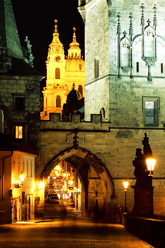 Romanesque and Gothic Malostranske bridge towers, with the two towers of Baroque St. Nicholas church beyond, at night, Mala Strana, Prague, Czech Republic, Europe