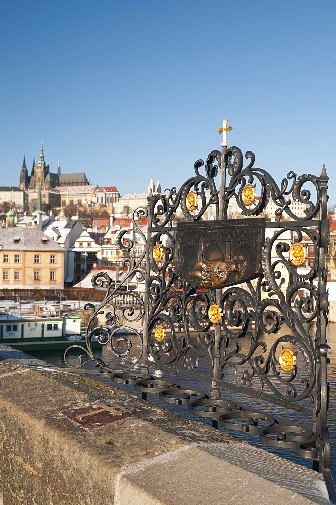 St. John of Nepomuk (Jan Nepomucky) shrine with cross at Charles Bridge with snow-covered Prague Castle and Mala Strana in background, UNESCO World Heritage Site, Prague, Czech Republic, Europe