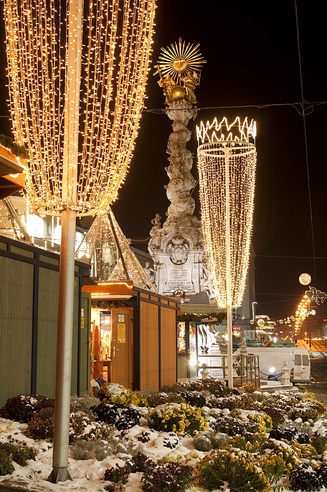 Snow-covered flowers, Christmas decorations and Baroque Trinity Column (Dreifaltigkeitssaule) at Christmas Market, Hauptplatz Square, Linz, Oberosterreich (Upper Austria), Austria, Europe