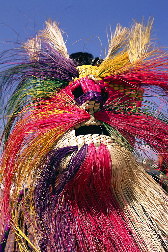 Head and shoulders portrait of a person wearing a brightly coloured straw mask, Oaxaca, Mexico, North America