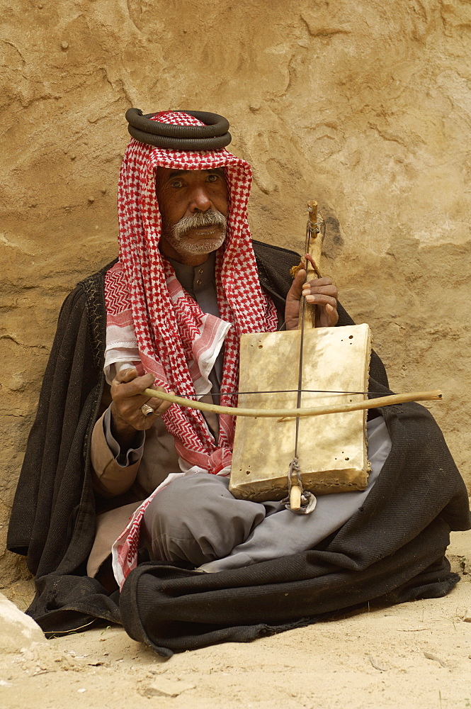 Bedouin man in traditional dress playing a musical instrument, Beida (Little Petra), Jordan, Middle East