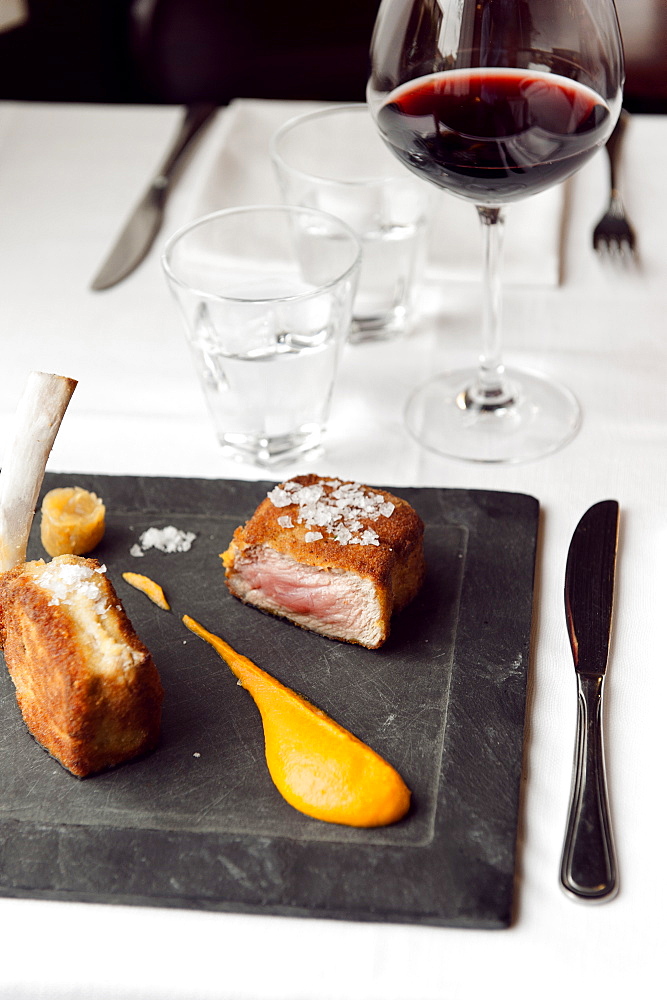 Cotoletta Milanese cooked by Restaurant Trattoria del Nuovo Macello served with a puree of carrots and cardamom and a fennel chutney on a plate of cast iron on one of the tables in the dining room of the restaurant Milan, Lombardy; Italy, Europe