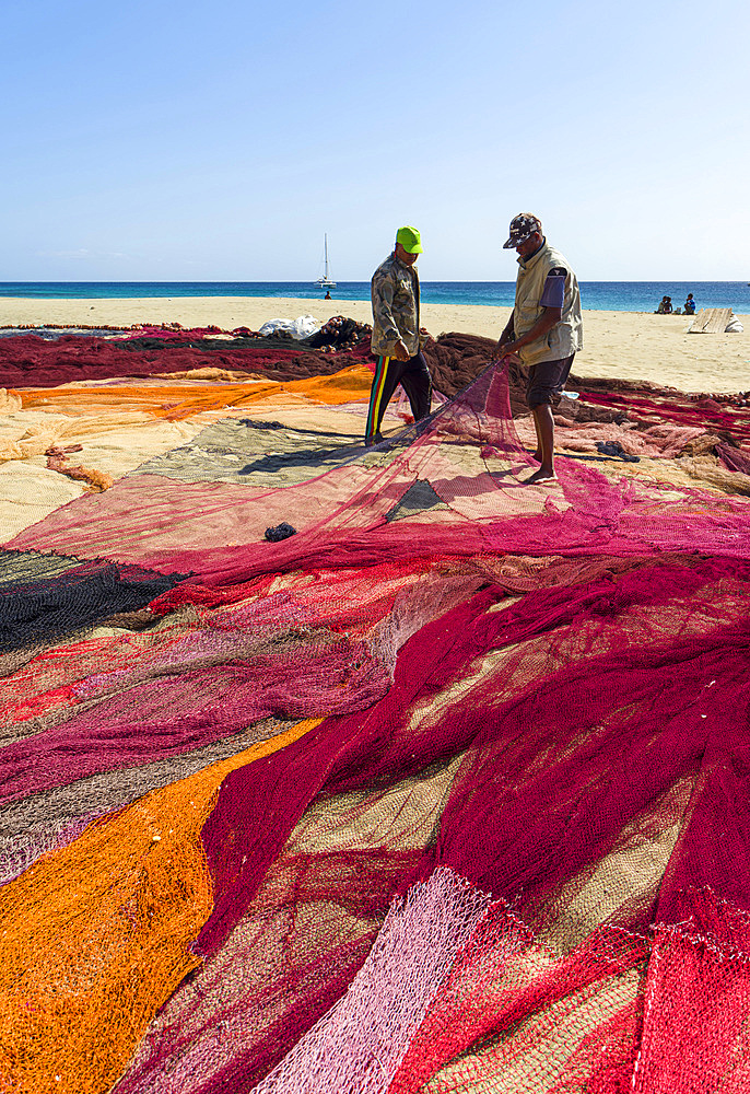 Fishermen are mending their colorful fishing nets on a beach near Sao Pedro. Island Sao Vicente, Cape Verde an archipelago in the equatorial, central Atlantic in Africa.