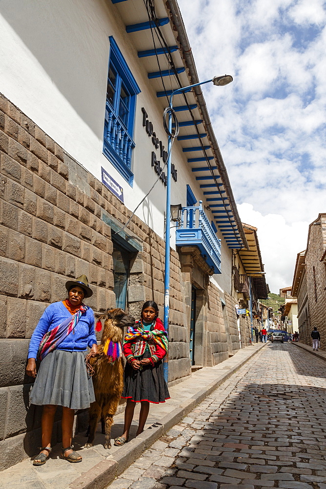 Women with traditional dress along Tupac Yupanqui Palace Hotel wall with its gray andesite blocks on San Agustin street, Cuzco, UNESCO World Heritage Site, Peru, South America