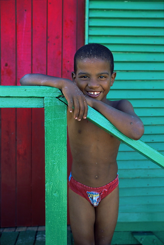 Young boy stands by colourfully painted Victorian bathing hut in False Bay, Cape Town, South Africa, Africa