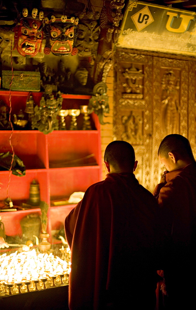 Monks light butter lamps on an auspicious night, watched by two fearsome masks, Boudha stupa, Bodhnath, Kathmandu, Nepal.