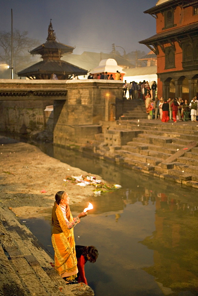 Two women making offerings (puja) before dawn by the Bagmati river, outside the Shiva temple during the Hindu festival of Shivaratri, Pashupatinath, Kathmandu, Nepal, Asia