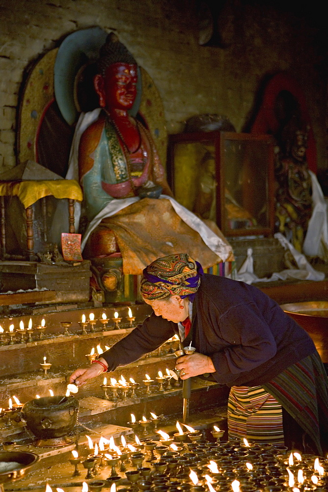 Old woman lighting butter lamps in a small temple on the north side of Boudha or Bodhnath stupa, Tibetan New Year (Lhosar), Kathmandu, Nepal, Asia